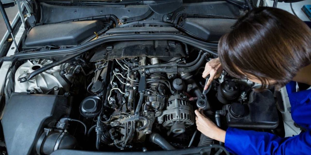 Szerelő nyitott motorháztetőnél dolgozik, az autó motorterében alkatrészeket ellenőriz szerszámmal