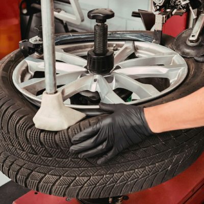 Szerelő fekete kesztyűben autógumit szerel le vagy fel egy alumínium felniről gumiszerelő gép segítségével egy autószervizben.