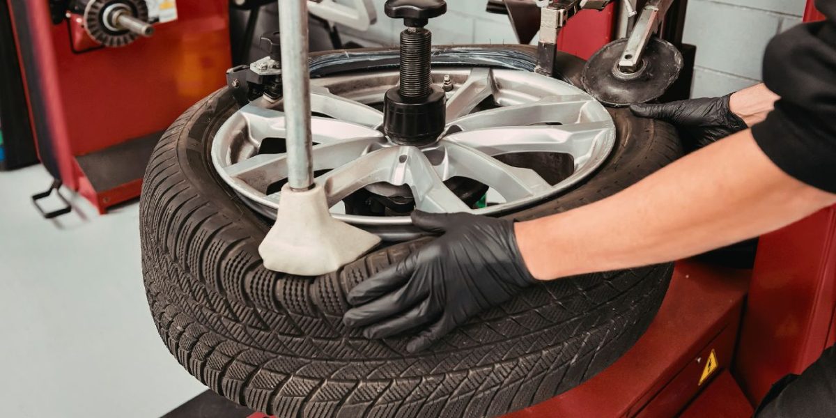 Szerelő fekete kesztyűben autógumit szerel le vagy fel egy alumínium felniről gumiszerelő gép segítségével egy autószervizben.